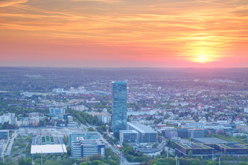 Naklejka na ściany i meble Elevated view of modern European city commercial / business district at sunset with glass and concrete office buildings, high tower blocks in outskirts under orange sky, Moosach Munchen Germany Europe