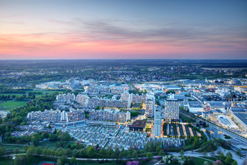 Modern European city outskirts aerial view in blue hour at dusk, concrete high-rise buildings and parks of dense housing complex with industrial commercial area in background, Munchen Germany Europe