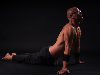 Buddhist monk practicing yoga on black background in long pants and glasses