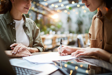 Close-up of serious businesswoman sitting at table and signing contract with personal manager after...