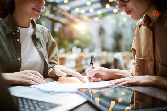 Close-up of content busy women signing contract after meeting: lady pointing at place for signature while working with client in cafe