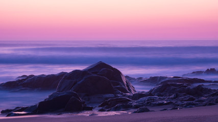 Long exposure shot at dusk over the ocean with sandstone rocks on the beach