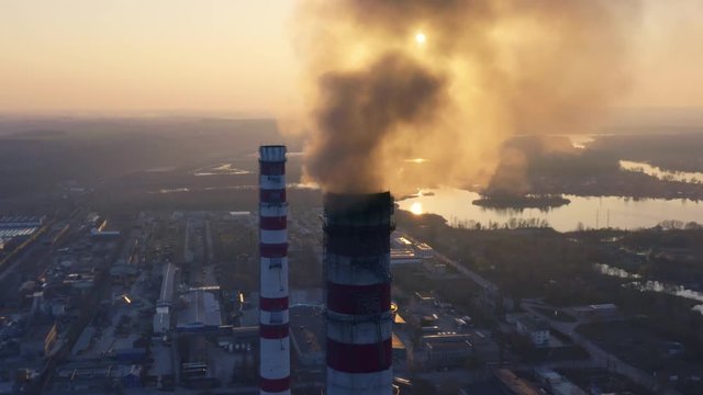 Aerial circling view of smoking chimneys of CHP plant (coal-fired power station) at sunset