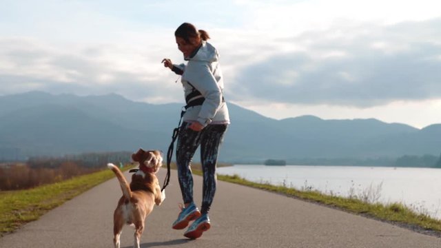 Young female fooling around with her beagle dog during a morning jogging 