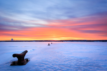 Snowy boat dock with colorful sky. Boat anchors in foreground. 