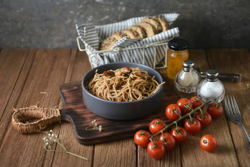 Tasty Italian spaghetti pasta with mussel, tomato, whole wheat bread and garnish on round dish and wooden plate for serving on wooden table background. side view,perspective, horizontal, image