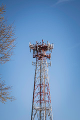 A tall metal cellular tower with a tree set on a clear blue sky background.