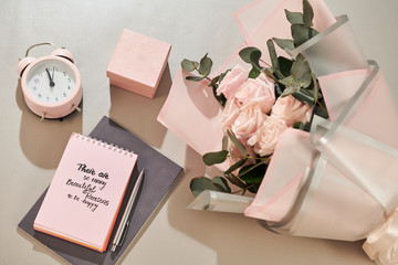 Gift box, alarm clock and pink rose flowers on white table top view in flat lay style. Greeting card for Mother or Woman day.