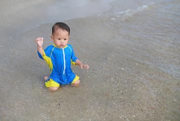 Portrait of Asian baby boy in swimming suit sitting on the sand beach.