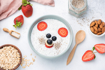 Healthy breakfast for kids with funny face food art. Chia pudding with almond milk, oats and berries. Top view