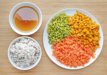 Chopped vegetables with soup and crush fish on white plate against wooden board background.