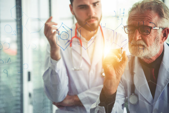 Senior scientists drawing chemical formulas on clear glass board and young scientists are watching - Powered by Adobe