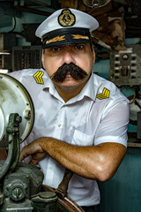 A sailor officer - old salt in the uniform is steering the ship with a rudder. Captain standing in the wheelhouse of ship and looking to camera. © milkovasa
