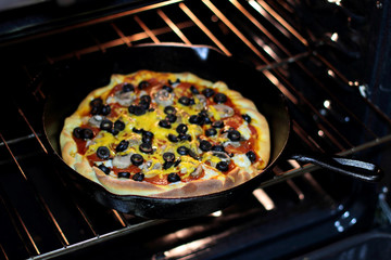 Freshly baked homemade pizza with pepperoni, mushrooms, and black olives in cast iron pan from the oven.