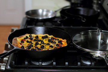 Freshly baked homemade pizza with pepperoni, mushrooms, and black olives in cast iron pan from the oven.