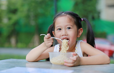 Adorable little Asian kid girl eating Instant noodles in the morning at the garden.