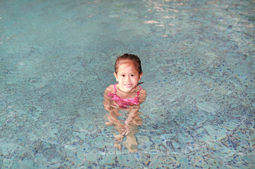 Fototapeta na wymiar Smiling little Asian kid girl playing alone in pool.