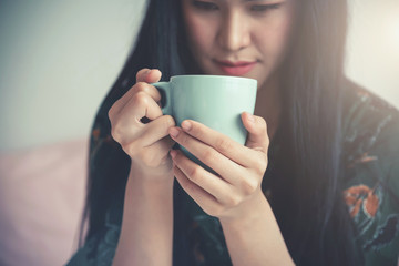Fototapeta premium Young asian woman holding a cup sitting on a bed in the room