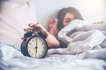 woman lying on the bed hold a clock, wake up concept.