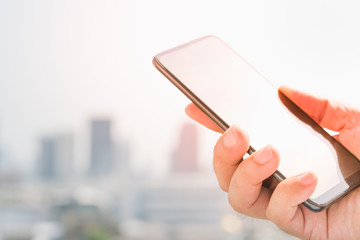 Man's hand hold/touch and looking at smart phone with cityscape using as background or backdrop.