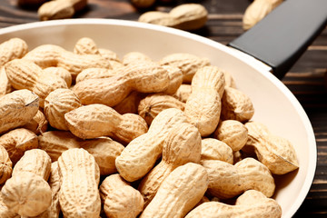  Frying pan with roasted peanuts on a wooden background. Place for text. Top view.