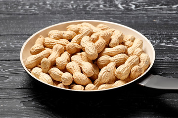Roasted peanuts in a pan on a black wooden background