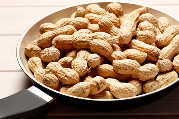 Frying pan full of fried tasty peanuts on a white wooden background with place for text. Close-up.