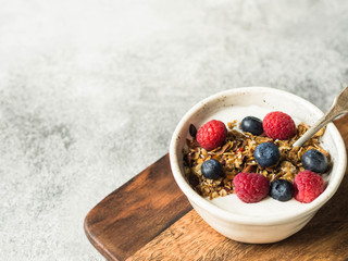A white bowl of homemade granola, yogurt, fresh berries on wood board. Vegetarian food, healthy breakfast