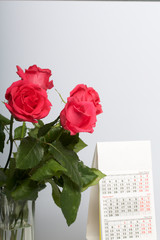 A bouquet of scarlet roses in a glass vase. Next is a calendar. On a white background.
