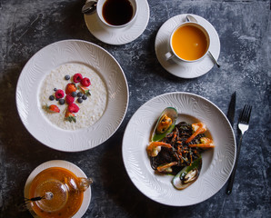 Menu at the cafe, Breakfast and lunch, Porridge with berries and pasta with seafood, Bulgur and black spaghetti with shrimps. Flatlay, Top view, Moody on black background, Darkstyle