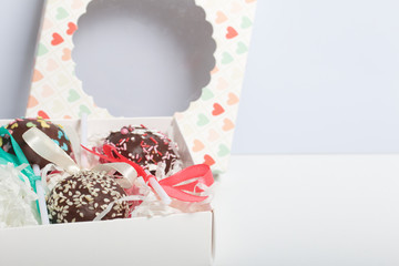 Cake pops are beautifully packed in a gift box. Nearby there is a cover with a transparent window. On a white background.