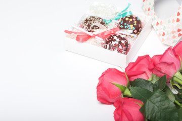 Obraz na płótnie Canvas Cake pops are beautifully packed in a gift box. Nearby there is a cover with a transparent window and a bouquet of scarlet roses.