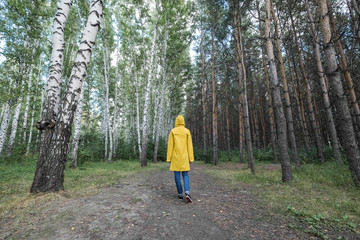 A woman in a yellow raincoat in the woods.