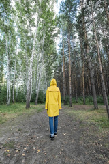 A woman in a yellow raincoat in the woods.