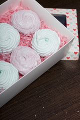 Homemade marshmallows of different colors are beautifully packed in a gift box. Nearby is the lid of the box with a transparent window. On a dark background.