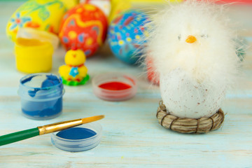 Easter eggs on multicolor wooden background with baby chicken, paints and brush