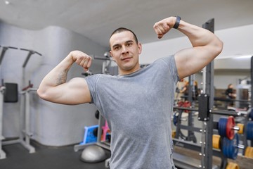 Young strong smiling muscular man in gym showing strong muscular arms.