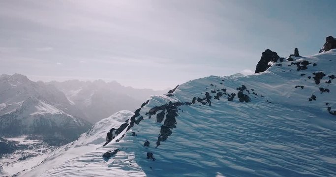 Aerial, drone shot, flying over a rocky mountain ridge, surrounded by snowy alpine mountains, revealing lots of wintry alp peaks, on a sunny, winter day, in the Swiss alps, in Switzerland