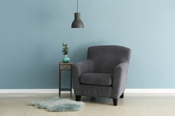 Soft armchair with small table near color wall in room