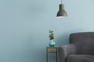 Soft armchair with small table and lamp on color background