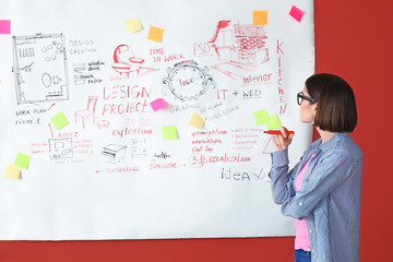 Fototapeta premium Female designer near big paper sheet with project plan in office