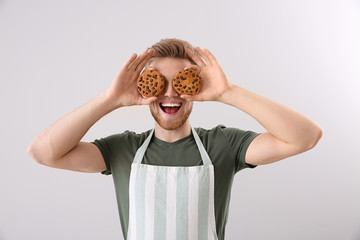 Happy male baker with fresh cookies on light background