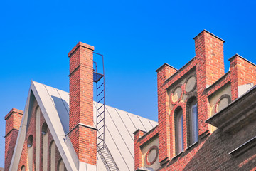 Fototapeta na wymiar Red brick chimney on the roof, fragment of the facade of a brick building against the blue sky