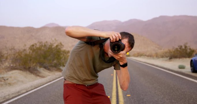 Young trendy male photographer bend over taking photo - desert background