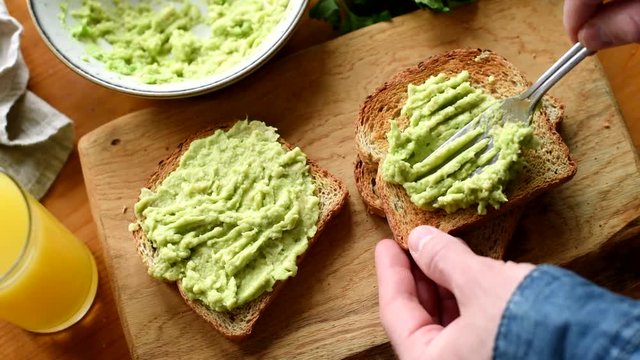 Making avocado toast. Man spread avocado on toasted sandwich bread. Top view