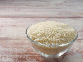 White basmati rice in a glass bowl on a brown wooden background