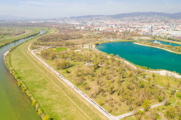 Fototapeta premium Zagreb, Croatia, Jarun lake, beautiful green recreation park area, sunny spring day, panoramic view from drone, city in background