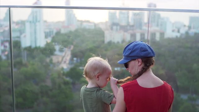Close shot of a two-year-old kid playing with his mother's braid on a delightful viewing platform. Pattaya, Thailand.