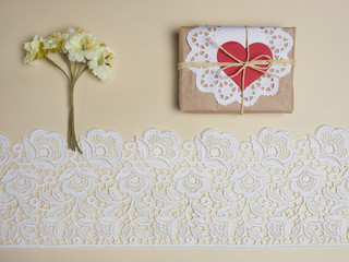 White lace on a beige background with a gift, red heart and flowers