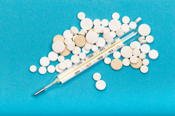 medical  thermometer and white pills on blue  background close up view